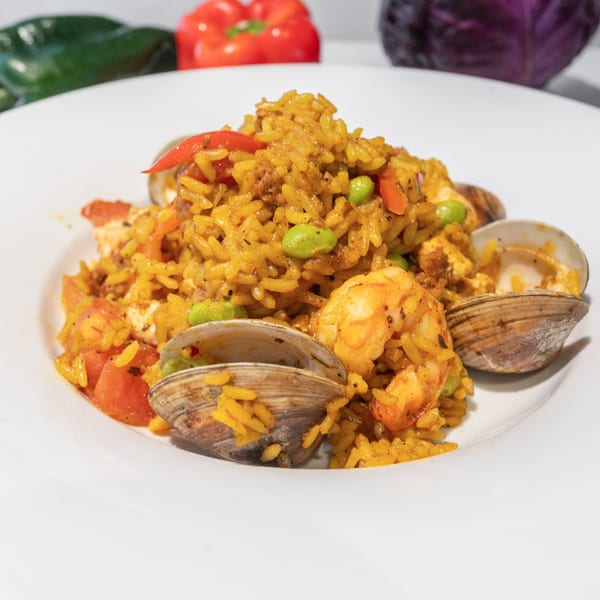 Close-up of a seafood paella dish with shrimp, clams, rice, and vegetables on a white plate.