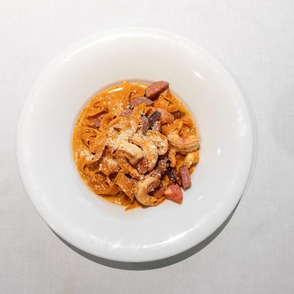 Pasta with shrimp, sausage, and parmesan cheese in a red sauce, served in a white bowl.