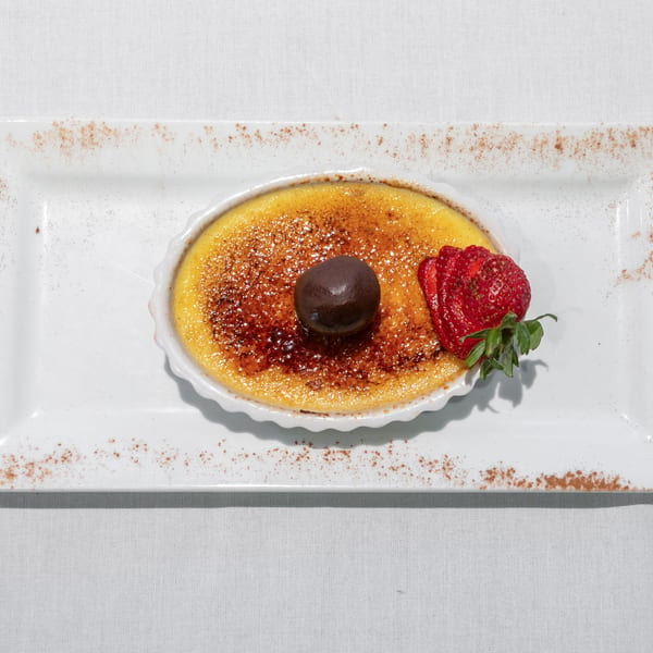 Crème brûlée in a white ramekin, garnished with a chocolate truffle and sliced strawberry.