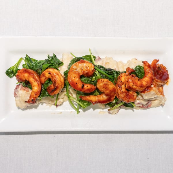 Grilled shrimp with fresh spinach and creamy mashed potatoes on a white rectangular plate.