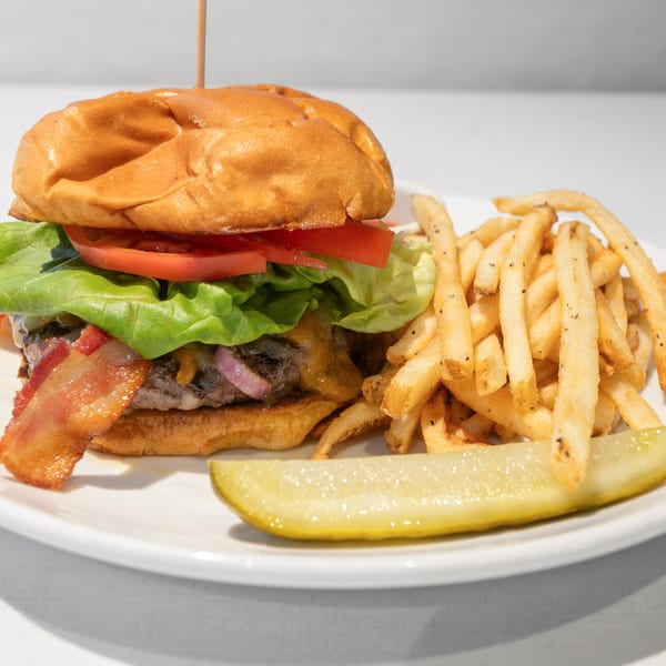 A bacon cheeseburger with lettuce, tomato, and red onion, served with fries and a pickle spear.
