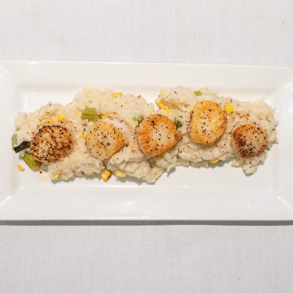 Five seared scallops with black pepper on a bed of risotto with corn and green vegetables.