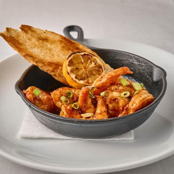 Sizzling shrimp in a black cast iron skillet, garnished with charred lemon and toasted bread.