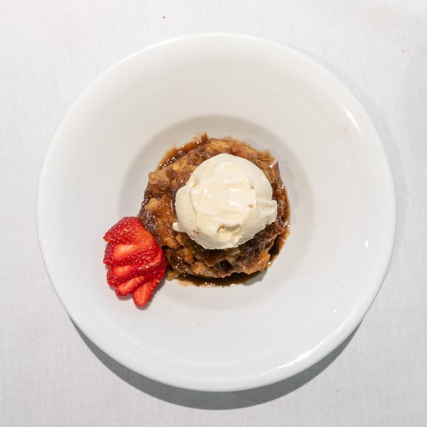 Warm apple cobbler topped with a scoop of vanilla ice cream and sliced strawberries in a white bowl.