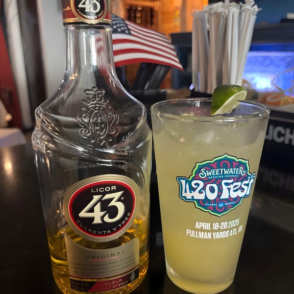 A bottle of Licor 43 and a Sweetwater 420 Fest drink with a lime wedge on a bar.