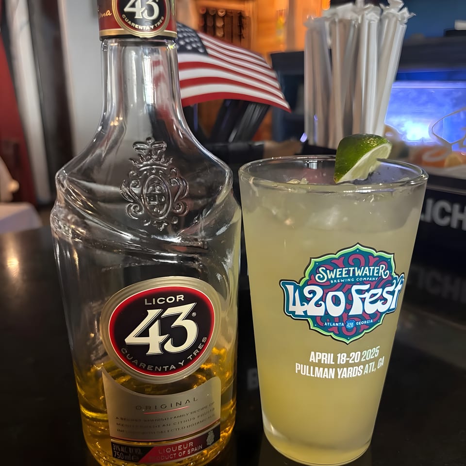 A bottle of Licor 43 and a Sweetwater 420 Fest drink with a lime wedge on a bar.