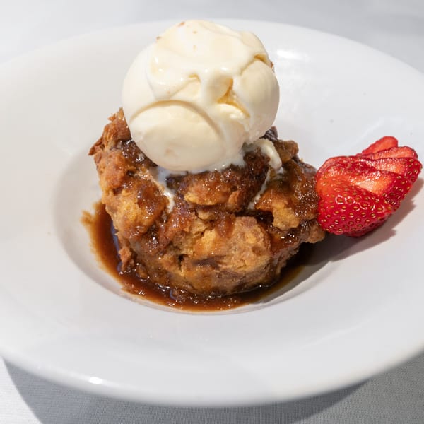 Warm bread pudding with vanilla ice cream and sliced strawberries on a white plate.