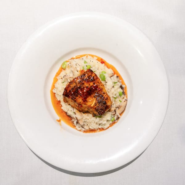 Pan-seared fish with a spicy glaze, served over risotto with peas and mushrooms in a white bowl.