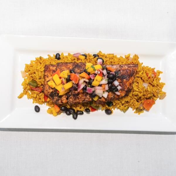 Grilled salmon with mango salsa and black beans on a bed of yellow rice, served on a white rectangular plate.