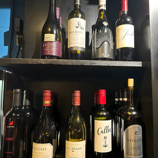 A dark shelf displays various wine bottles, including J. Lohr, Oberon, Josh, Meiomi, La Crema, Callia, and Sterling.