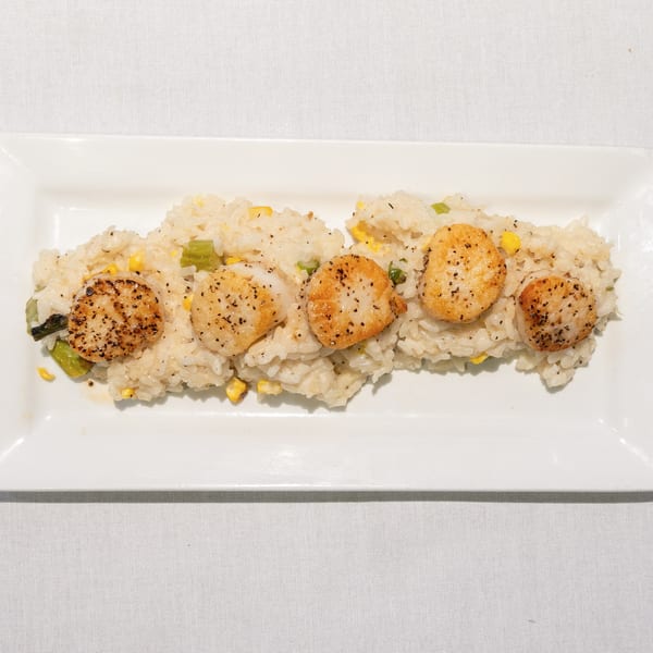 Five seared scallops with black pepper on a bed of risotto with corn and green vegetables.