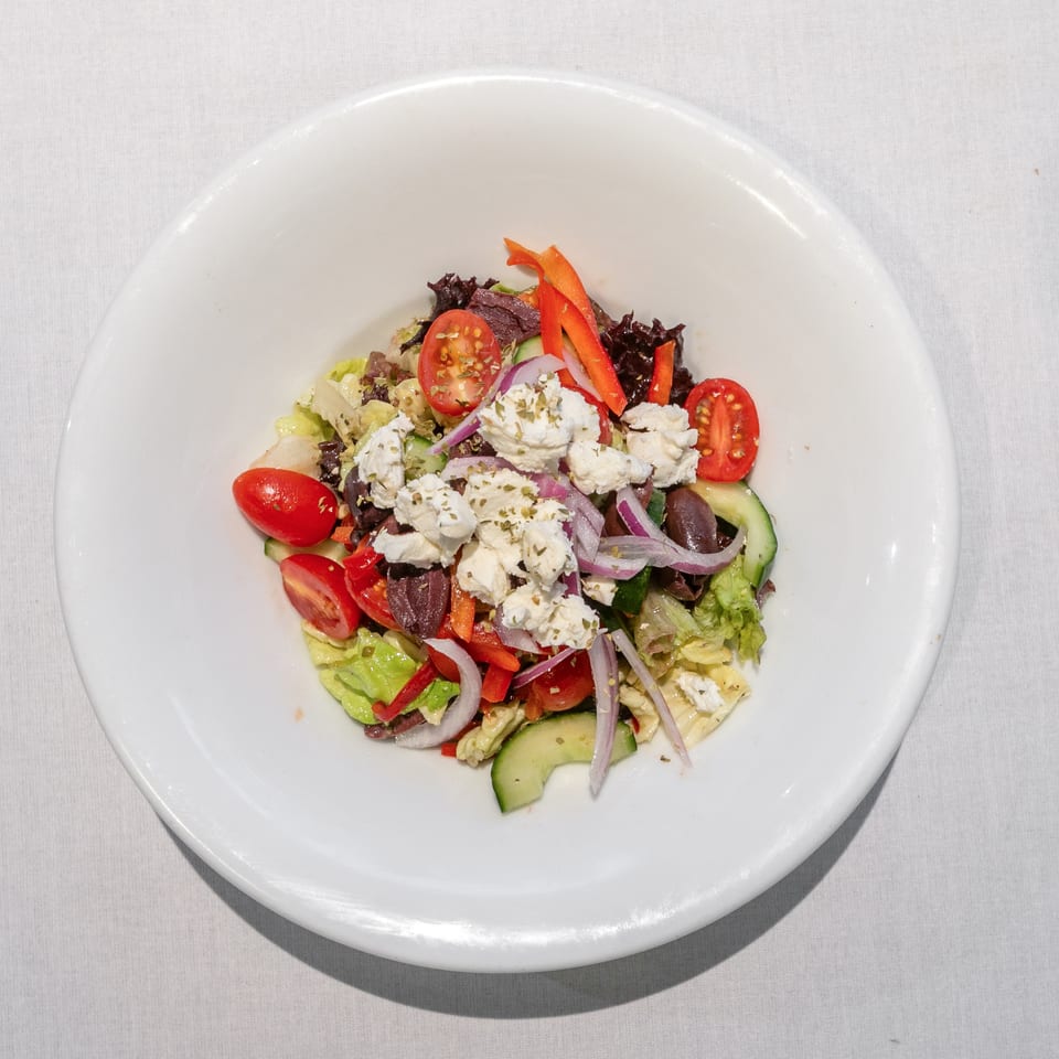 A vibrant Greek salad with feta, olives, tomatoes, cucumbers, and red onion in a white bowl.