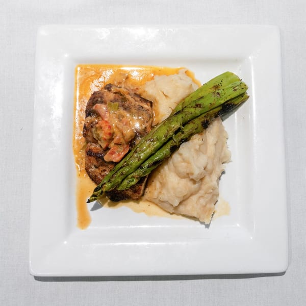 Grilled steak with crawfish sauce, mashed potatoes, and asparagus on a white rectangular plate.